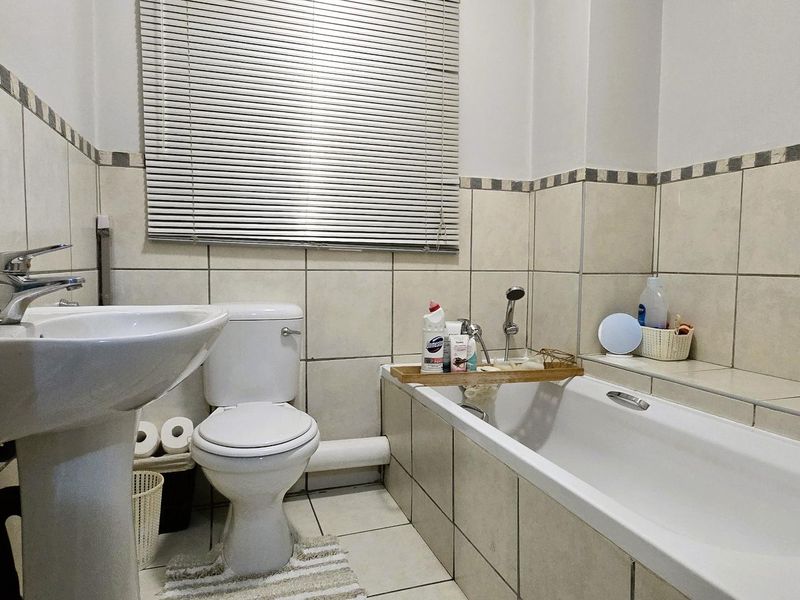 A functional bathroom featuring a pedestal basin, toilet, and bathtub with tiled walls and flooring, providing a clean and practical space.