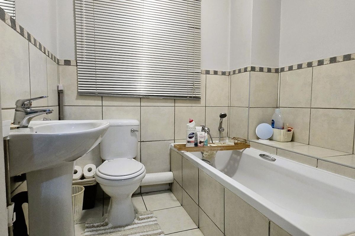 A functional bathroom featuring a pedestal basin, toilet, and bathtub with tiled walls and flooring, providing a clean and practical space.