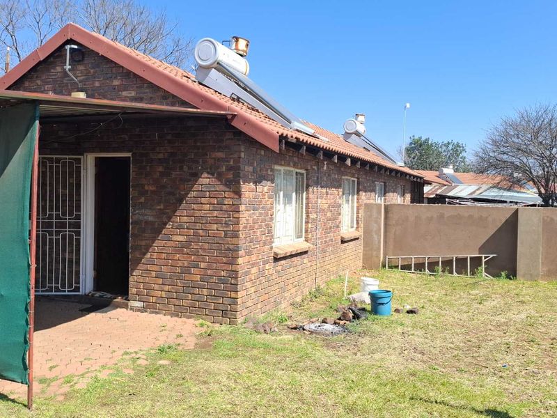 Rear view of a face brick house featuring a paved patio area, solar water heating system, and a private garden with boundary walling.