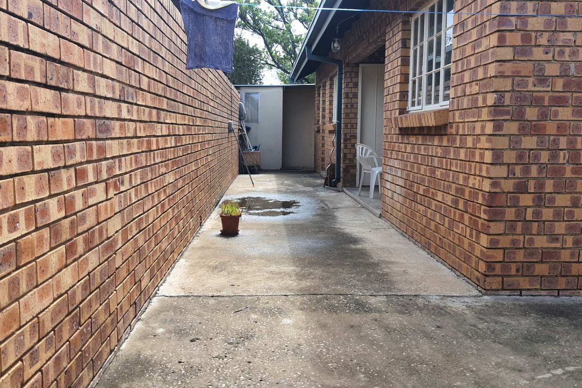 A narrow exterior side passage featuring exposed brick walls and concrete paving, providing access to the rear of the apartment building.