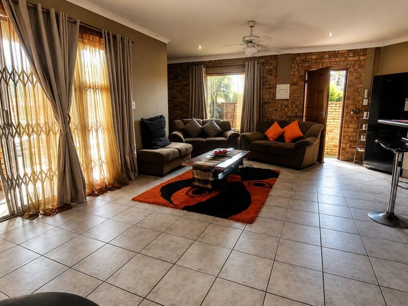 Spacious open-plan living area featuring tiled floors, an exposed brick feature wall, ceiling fan, and direct access to the outdoor area via sliding doors.