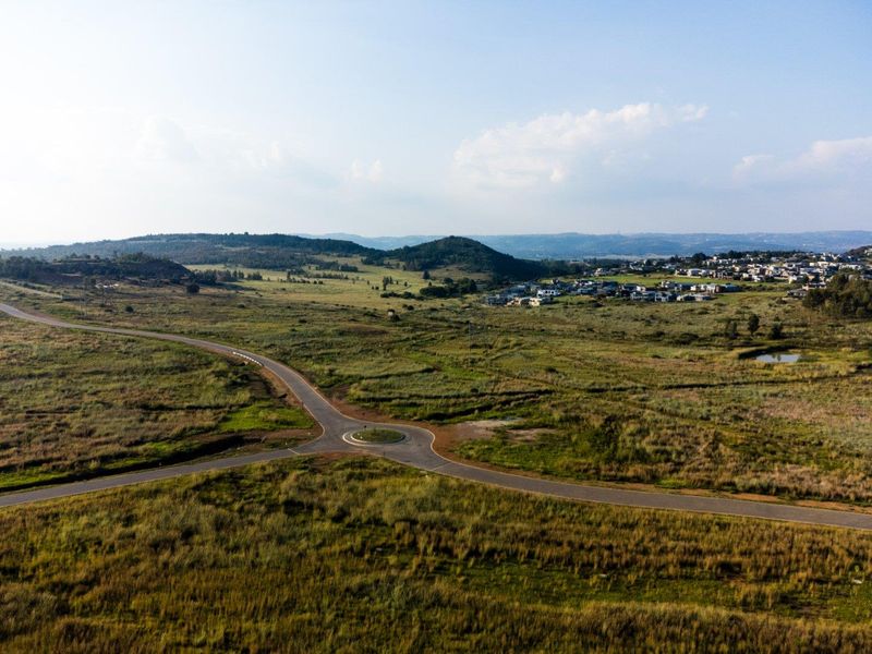 An aerial view of the surrounding landscape, featuring a paved road with a roundabout and distant residential development.