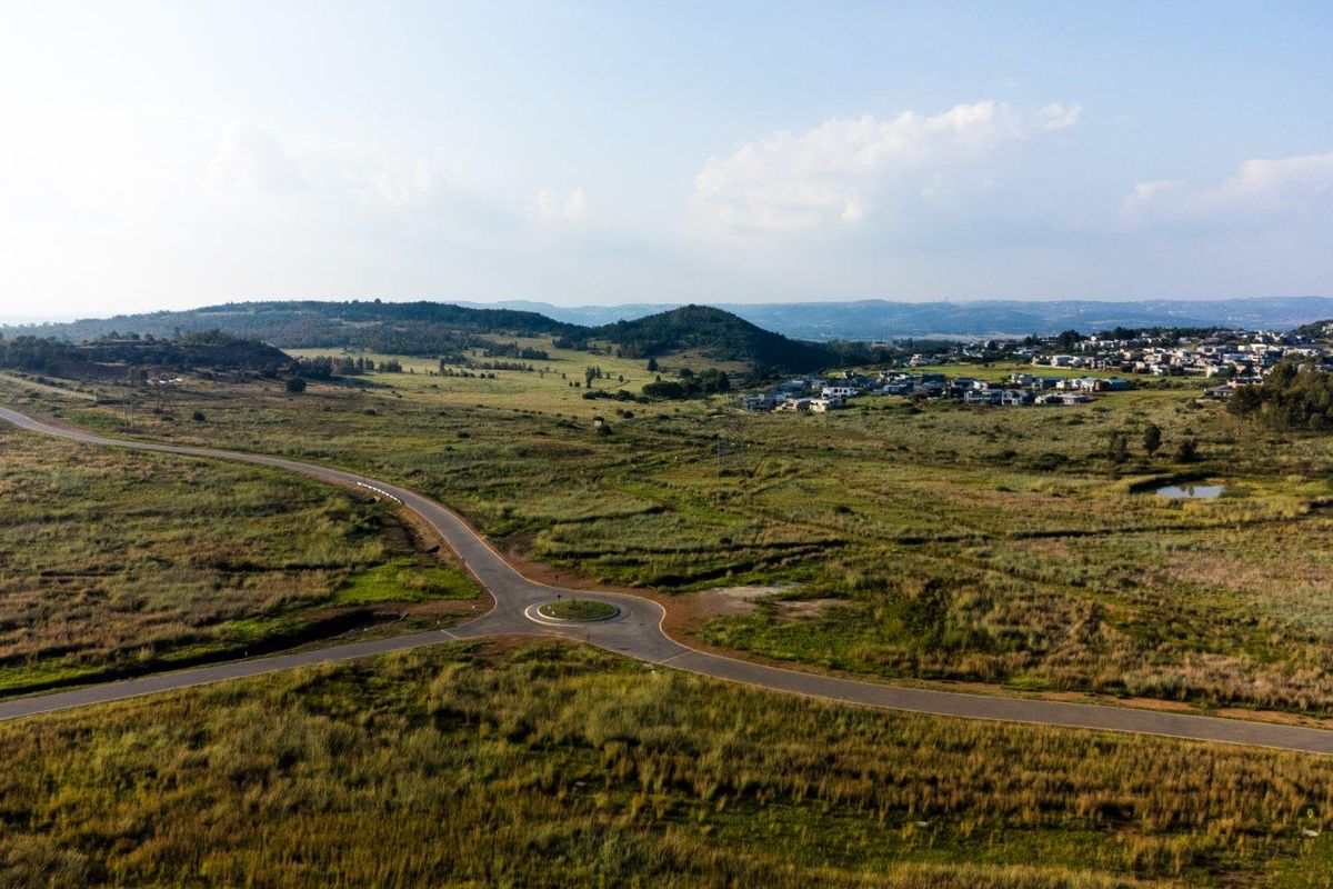 An aerial view of the surrounding landscape, featuring a paved road with a roundabout and distant residential development.