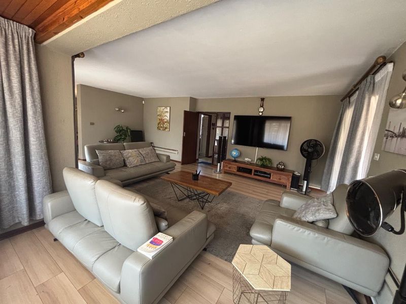 Spacious living room featuring light-toned laminate flooring, timber ceiling accents, and neutral wall finishes, providing a comfortable and functional family living space.