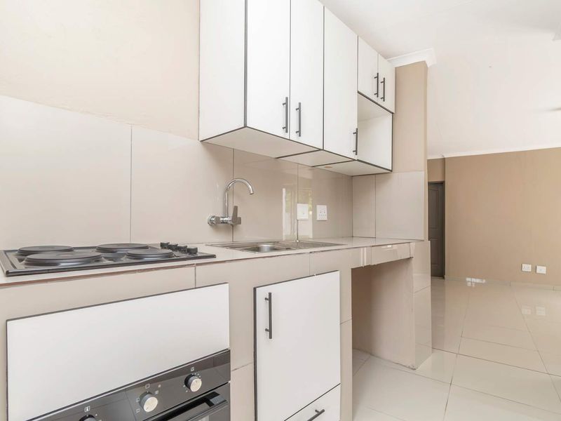 A clean, modern kitchen featuring white cabinetry, a built-in oven and hob, tiled backsplash, and neutral floor tiles in an open-plan layout.