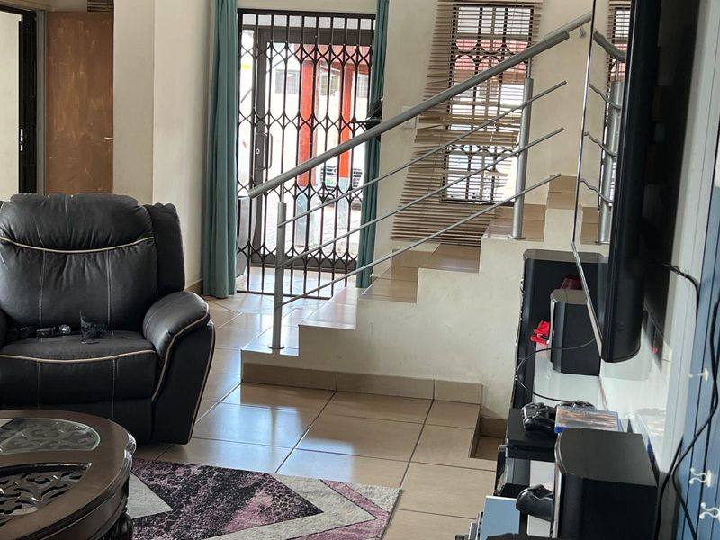 Living area featuring tiled flooring, a staircase with a modern stainless steel balustrade, and a security gate at the entrance.