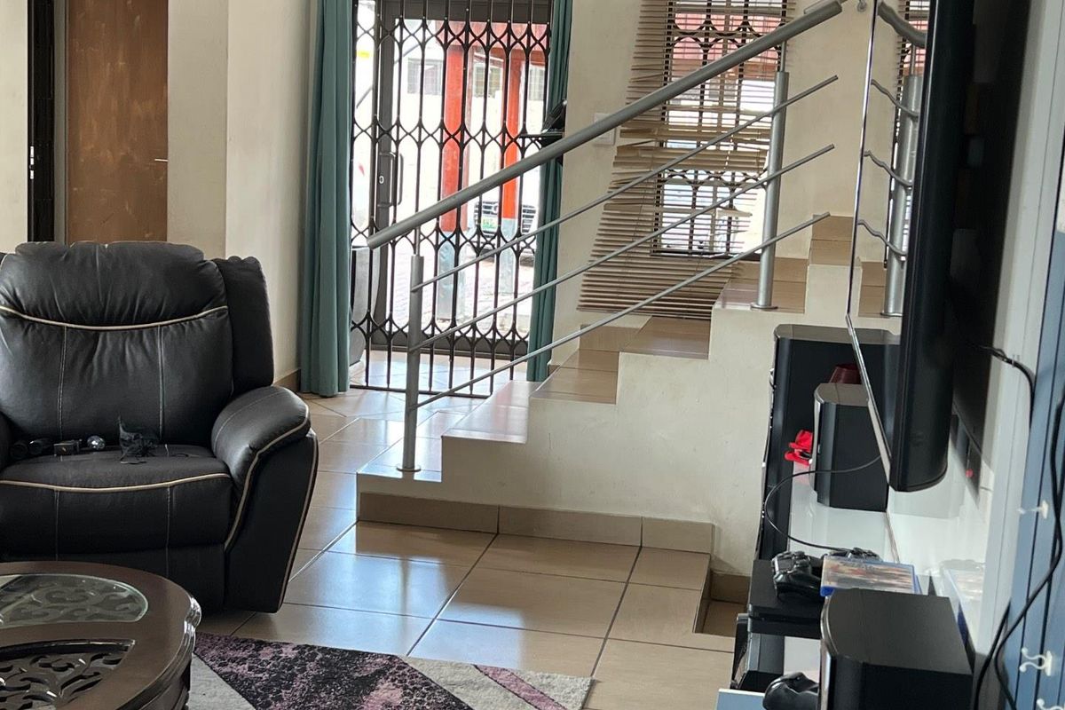 Living area featuring tiled flooring, a staircase with a modern stainless steel balustrade, and a security gate at the entrance.