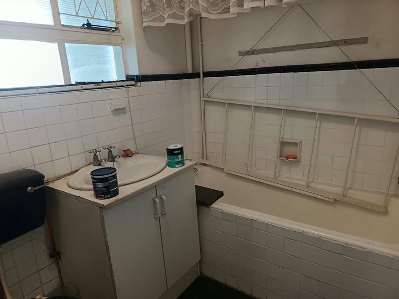 A dated bathroom featuring a vanity cabinet, ceramic basin, and bathtub with tiled walls, requiring renovation to update finishes and fixtures.