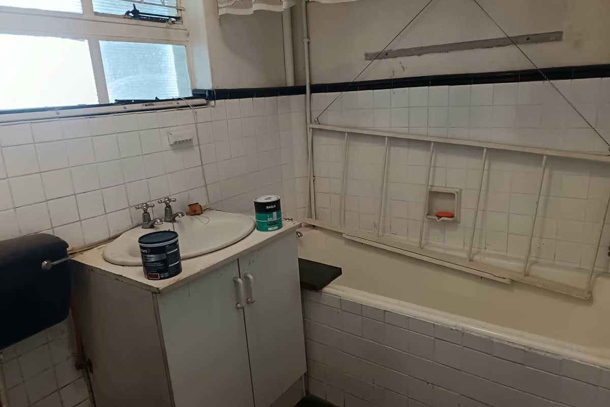 A dated bathroom featuring a vanity cabinet, ceramic basin, and bathtub with tiled walls, requiring renovation to update finishes and fixtures.
