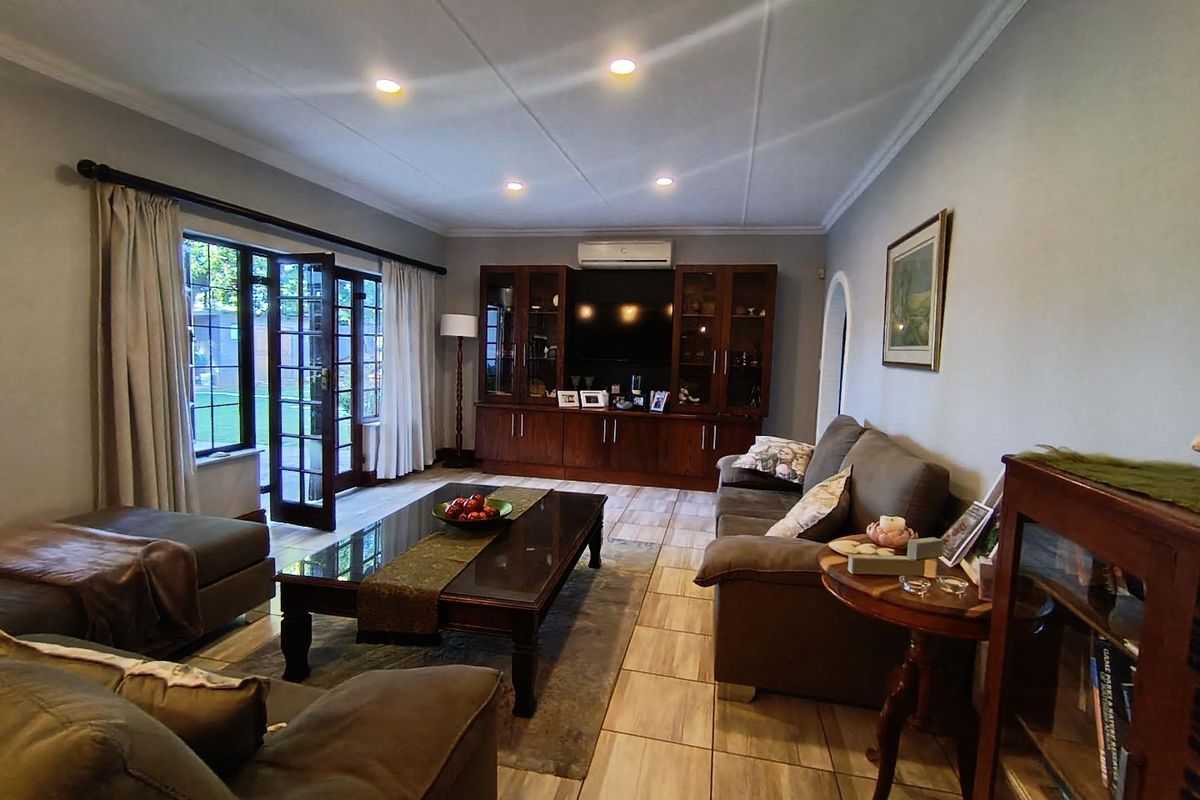 A spacious living room featuring tiled flooring, recessed ceiling lighting, a built-in wooden media cabinet, and French doors providing direct access to the garden.