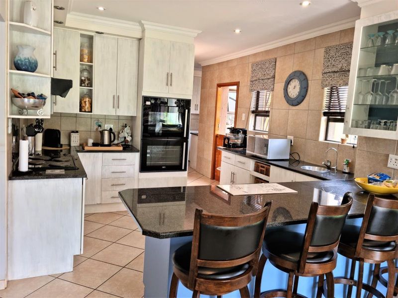 A well-appointed kitchen featuring granite countertops, a central island, built-in oven and hob, and ample cabinetry with a tiled splashback.