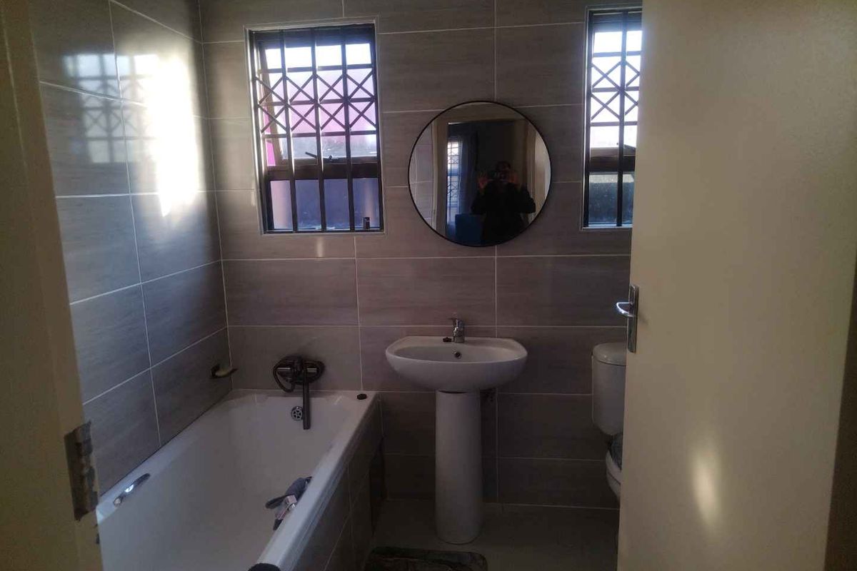 A clean, modern bathroom featuring tiled walls, a pedestal basin, a bathtub, and a toilet, with security bars on the windows.