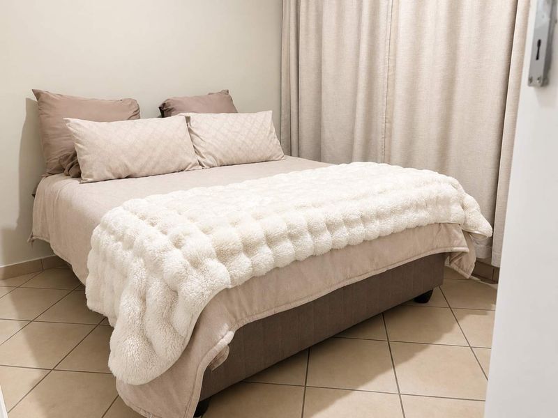 A well-maintained bedroom featuring neutral tiled flooring and full-length curtain tracks, offering a clean and comfortable living space.