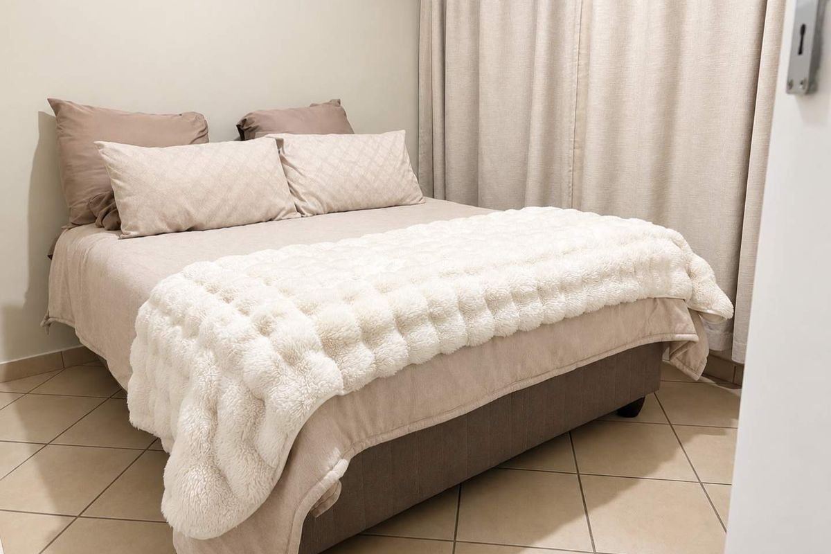 A well-maintained bedroom featuring neutral tiled flooring and full-length curtain tracks, offering a clean and comfortable living space.