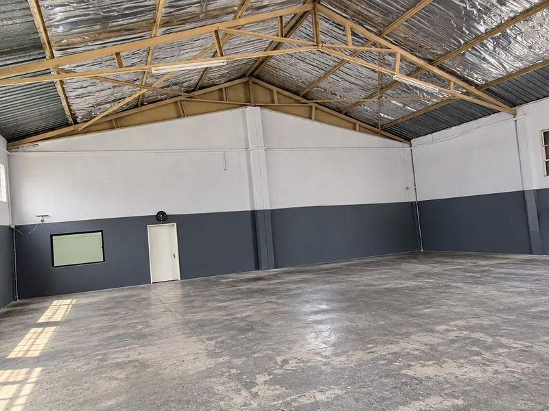 Spacious industrial warehouse unit featuring high ceilings with exposed steel trusses, concrete flooring, and ample natural light through large industrial windows.