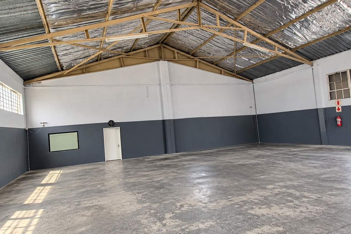 Spacious industrial warehouse unit featuring high ceilings with exposed steel trusses, concrete flooring, and ample natural light through large industrial windows.