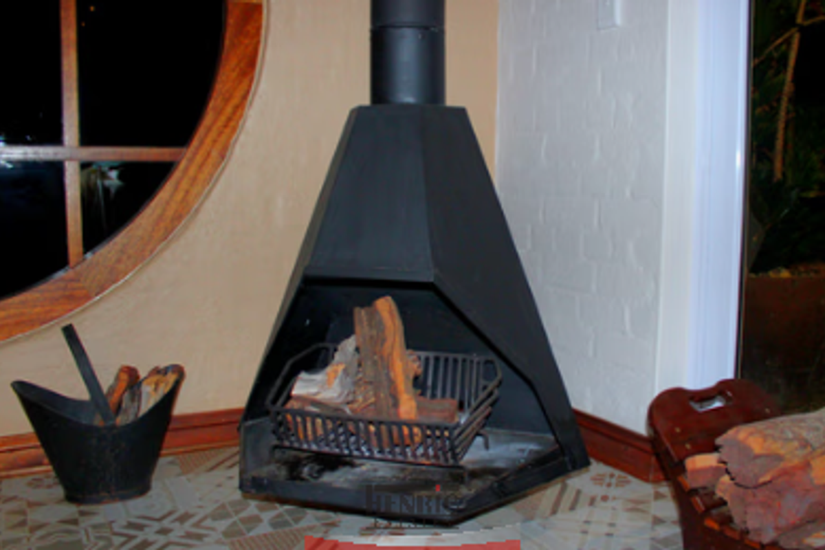 A freestanding black metal fireplace with a conical flue, set against a white brick wall with a unique circular window feature.