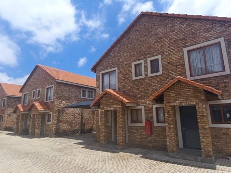 A row of face brick townhouses featuring tiled roofs, paved driveways, and covered entrances in a well-maintained residential complex.