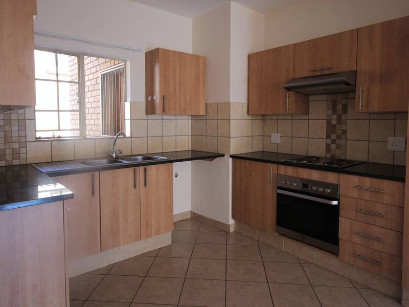 A functional kitchen featuring light wood-finish cabinetry, dark granite countertops, built-in oven, hob, extractor fan, and neutral tiled flooring.