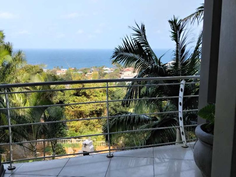 A covered balcony featuring tiled flooring and a stainless steel balustrade, offering expansive ocean and coastal views.