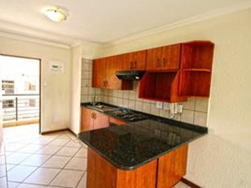 A functional kitchen featuring wooden cabinetry, granite countertops, a built-in hob with extractor fan, and direct access to an outdoor balcony area.