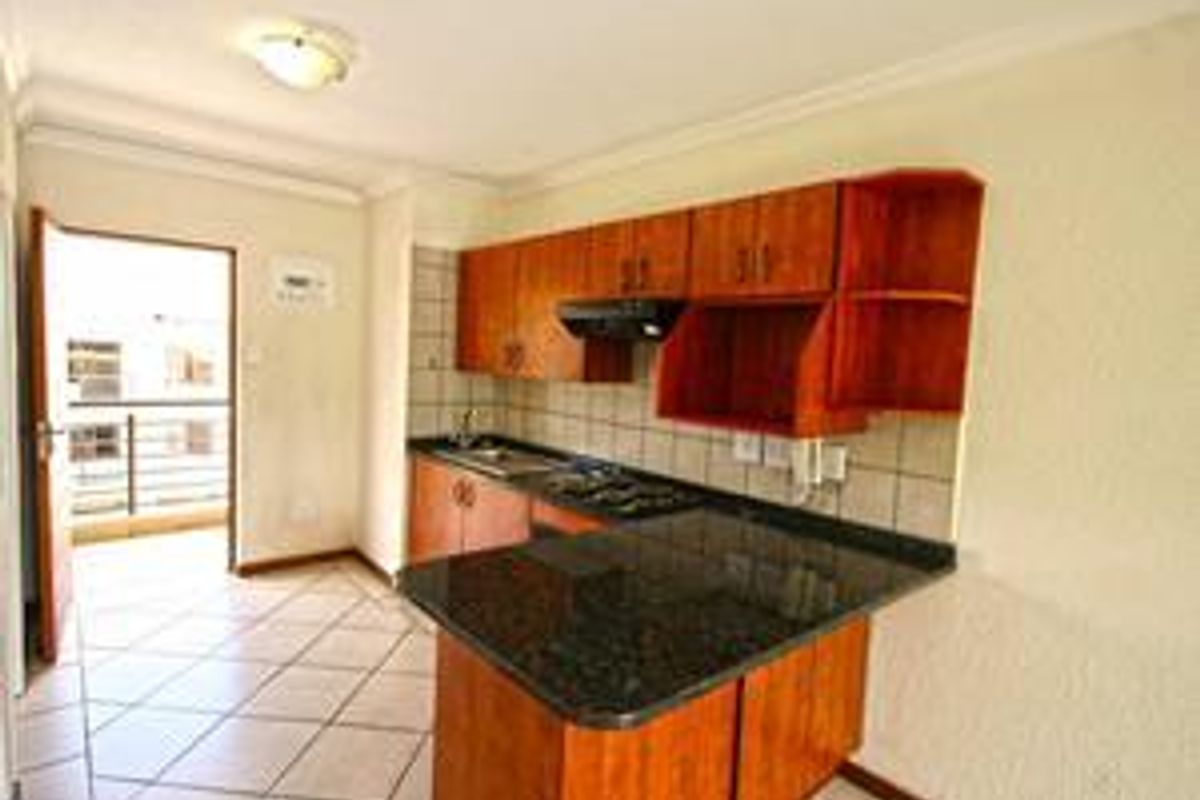 A functional kitchen featuring wooden cabinetry, granite countertops, a built-in hob with extractor fan, and direct access to an outdoor balcony area.
