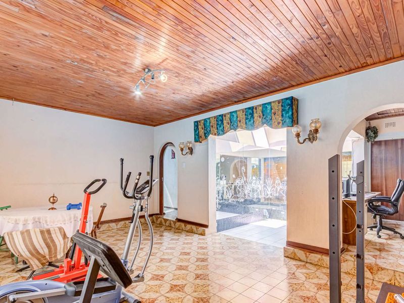 Spacious living area featuring a timber-clad ceiling, ceramic tiled flooring, and arched doorways leading to adjacent rooms.