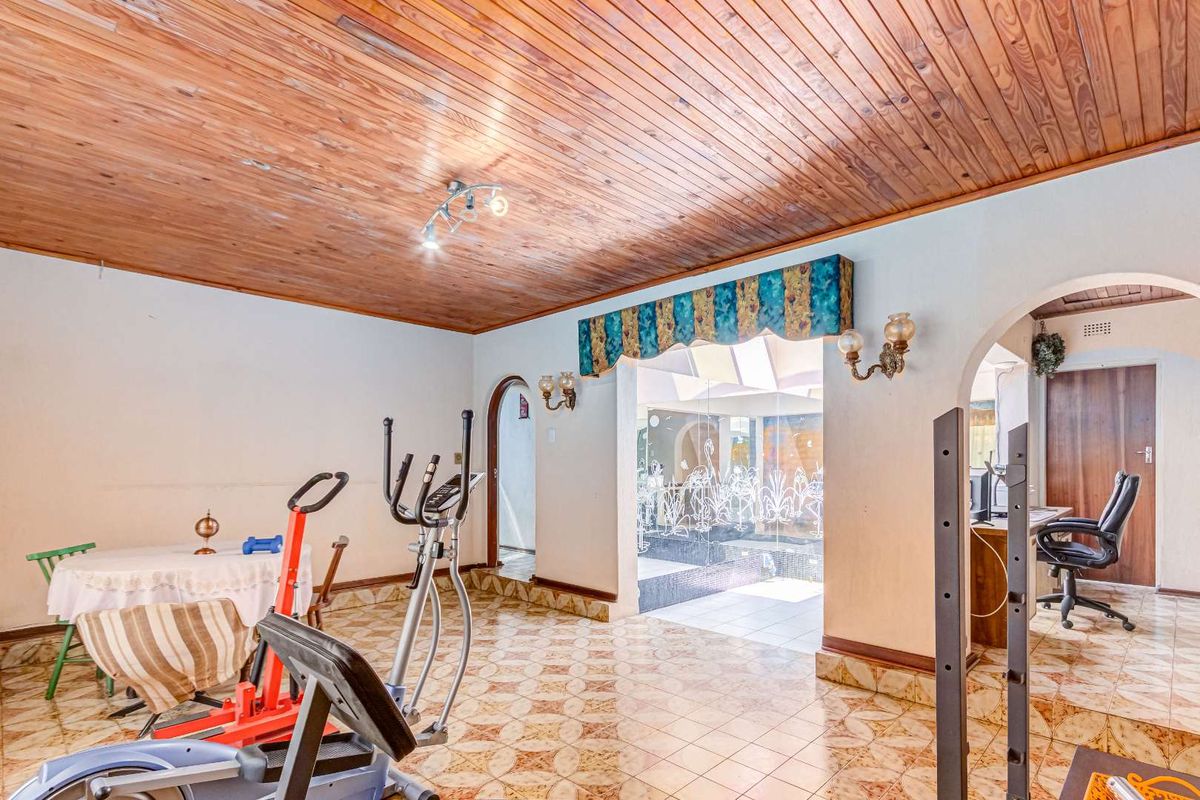 Spacious living area featuring a timber-clad ceiling, ceramic tiled flooring, and arched doorways leading to adjacent rooms.
