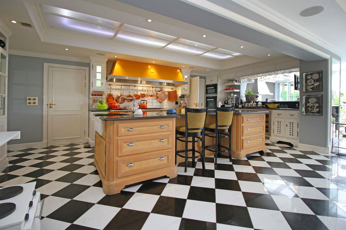 Spacious kitchen featuring a large central island, high-end built-in appliances, custom cabinetry, and distinctive black and white checkered flooring under a coffered ceiling.