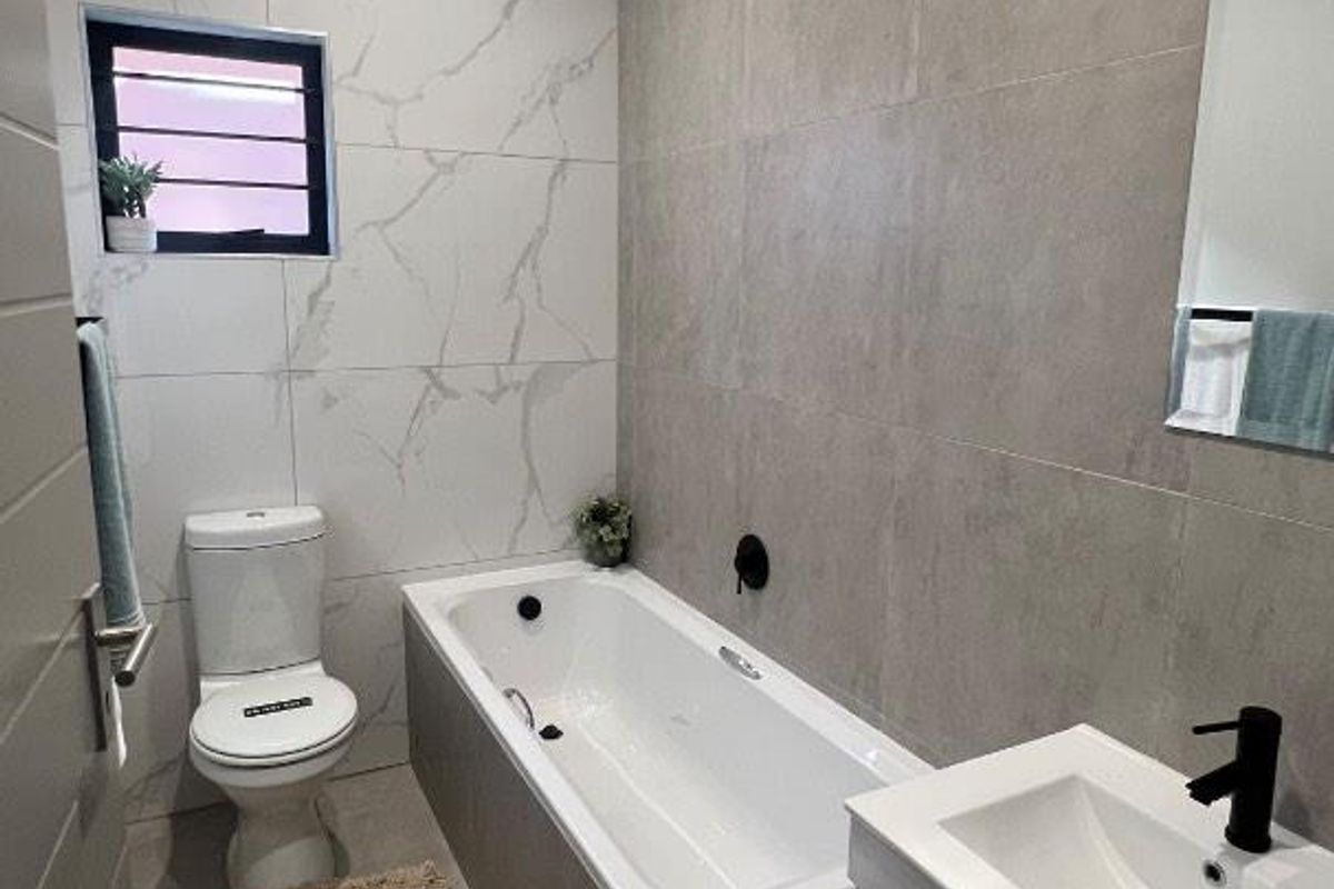 Modern bathroom featuring a built-in bathtub, wall-mounted vanity with matte black fixtures, and contemporary large-format wall tiling.