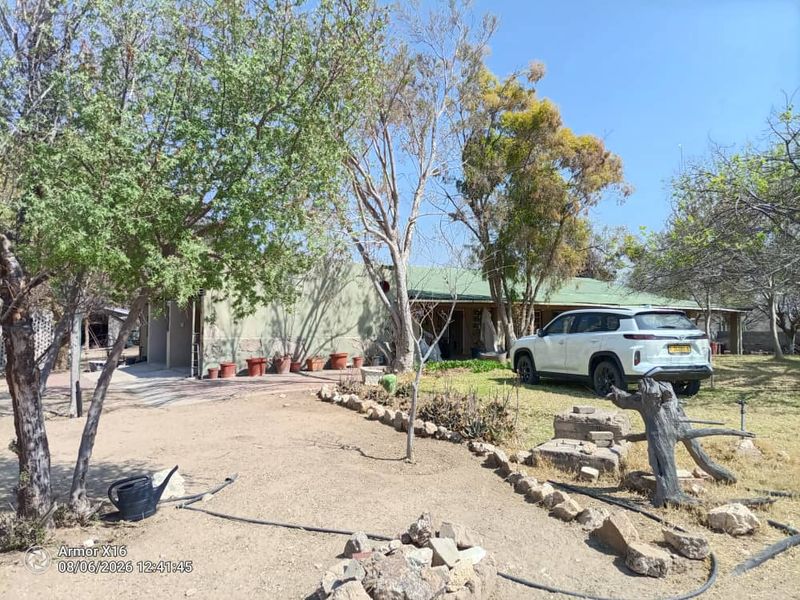 Front view of a small holding property featuring a single-story dwelling with a metal roof, covered patio, and established garden area.