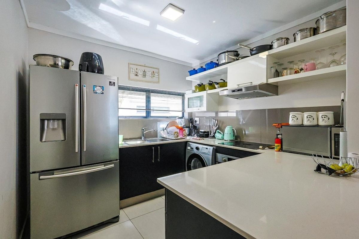 Modern kitchen featuring dark cabinetry, white stone countertops, integrated stainless steel appliances, and open shelving for storage.