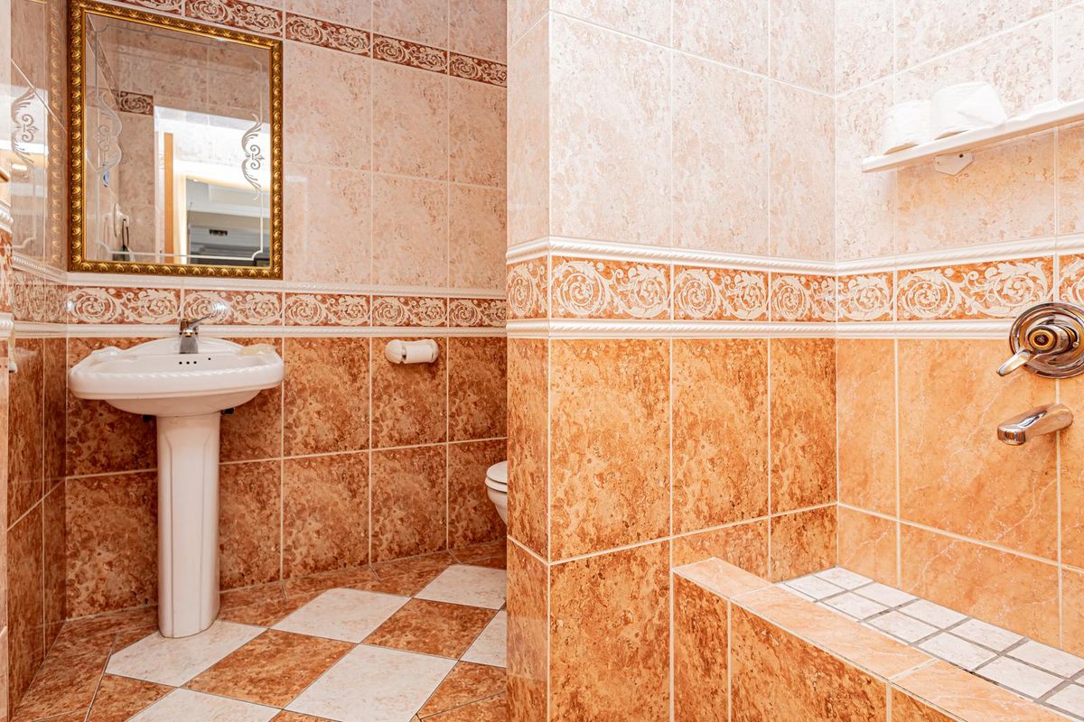 A bathroom featuring marble-style ceramic wall and floor tiles, a pedestal sink, and a built-in shower area with wall-mounted fixtures.