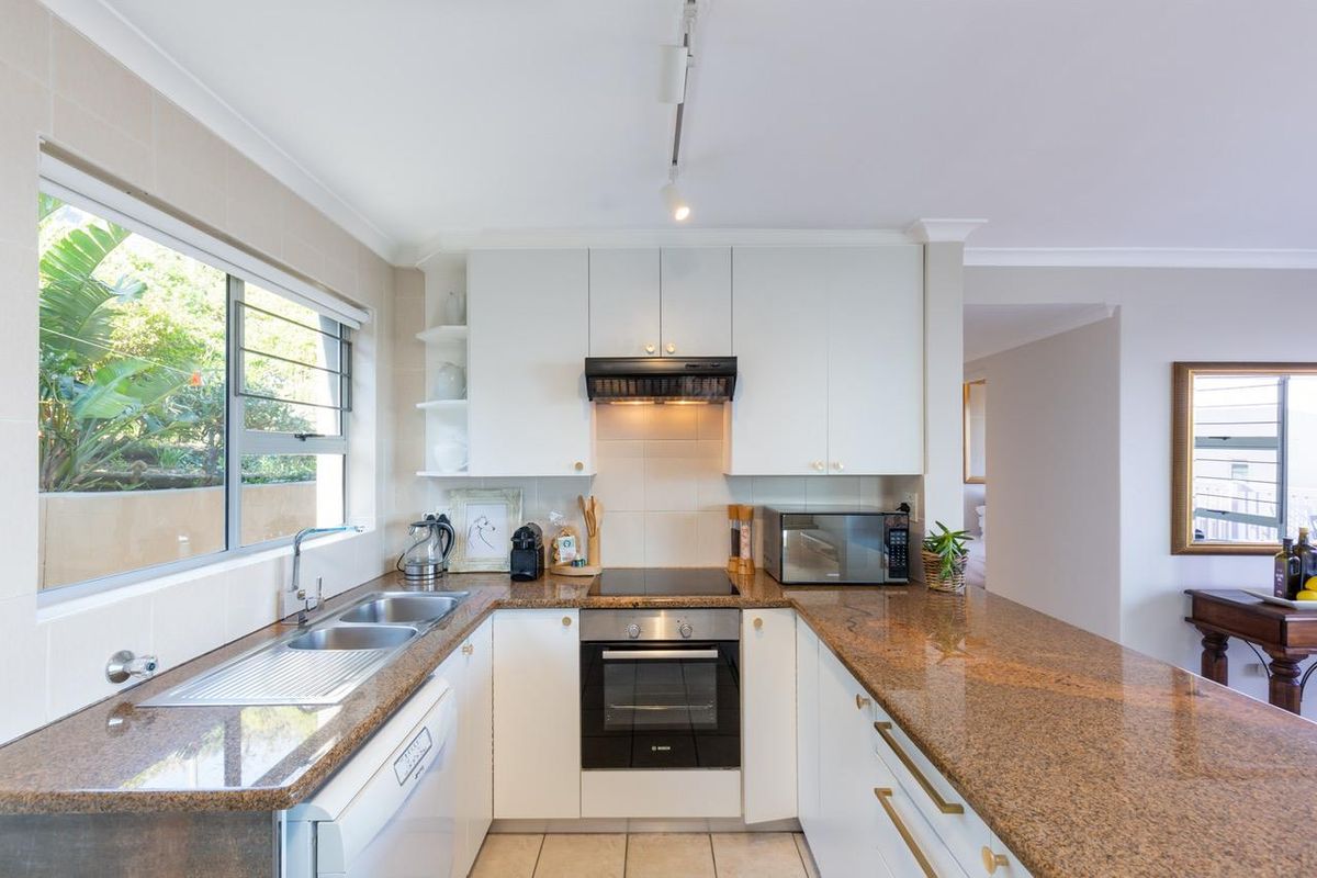 A functional kitchen featuring granite countertops, white cabinetry, built-in oven, electric hob, and a double bowl stainless steel sink with natural light.