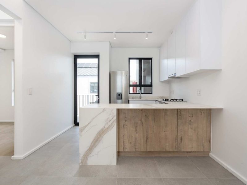 Modern kitchen featuring sleek white cabinetry, wood-grain accents, stone countertops, a gas hob, and integrated extractor fan, finished with neutral floor tiles.