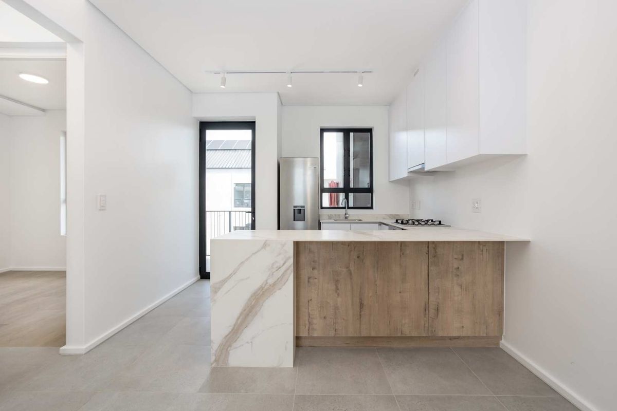 Modern kitchen featuring sleek white cabinetry, wood-grain accents, stone countertops, a gas hob, and integrated extractor fan, finished with neutral floor tiles.