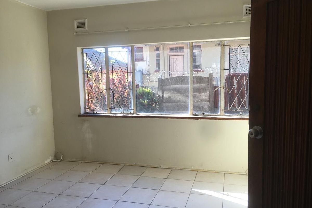 An empty bedroom featuring tiled flooring and large leaded glass windows, requiring cosmetic updates to the wall finishes and window frames.