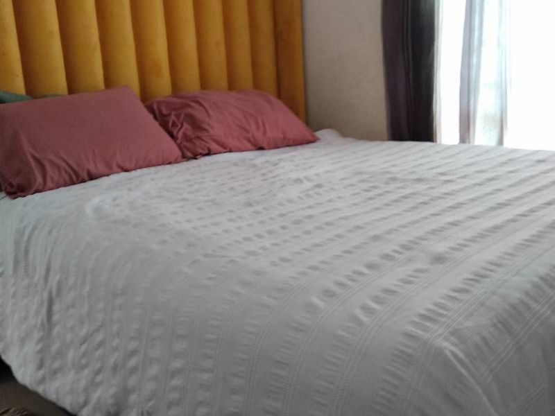 A bedroom featuring a large bed with a yellow upholstered headboard and window curtains.