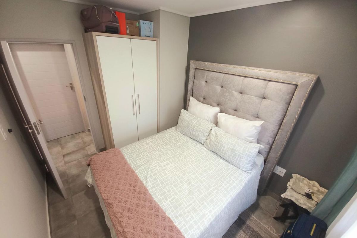 A compact bedroom featuring a built-in wardrobe, tiled flooring, and a neutral color palette with a feature wall.