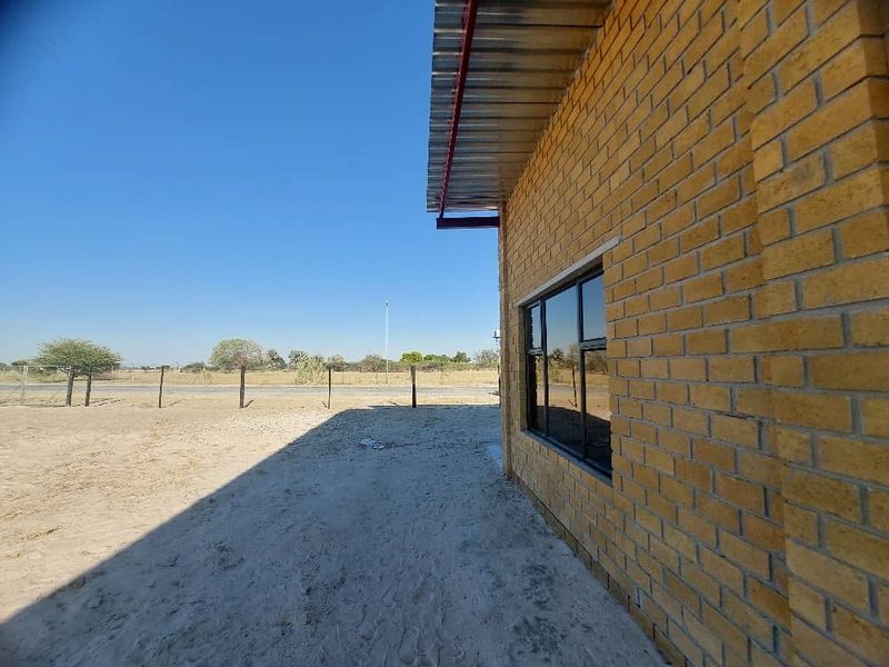 Side view of an industrial building featuring face brick construction, aluminium window frames, and a corrugated metal roof set on a sandy plot.