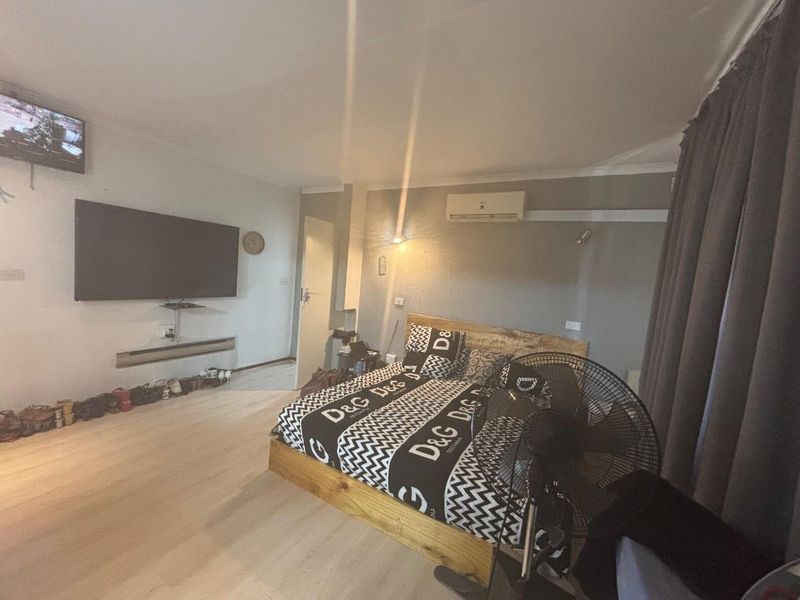 A bedroom featuring laminate flooring, coving, and a wall-mounted air conditioning unit.