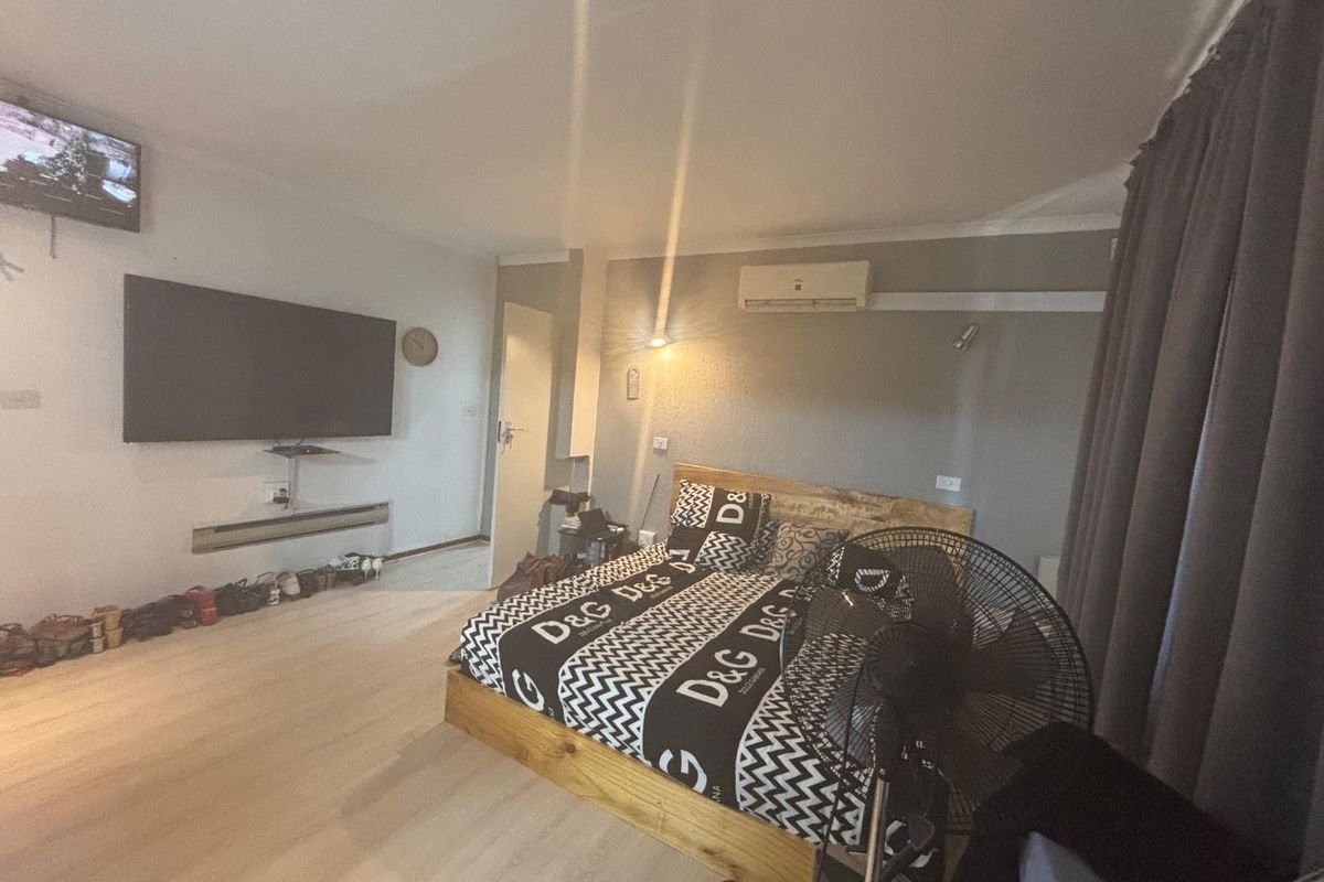 A bedroom featuring laminate flooring, coving, and a wall-mounted air conditioning unit.