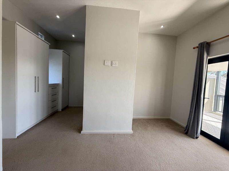 A spacious, neutral bedroom featuring built-in cupboards, recessed lighting, and a sliding glass door providing access to the exterior.