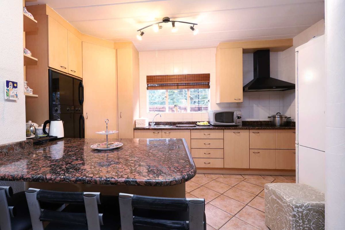 A functional kitchen featuring light wood cabinetry, granite countertops, a breakfast island, and a black extractor fan.