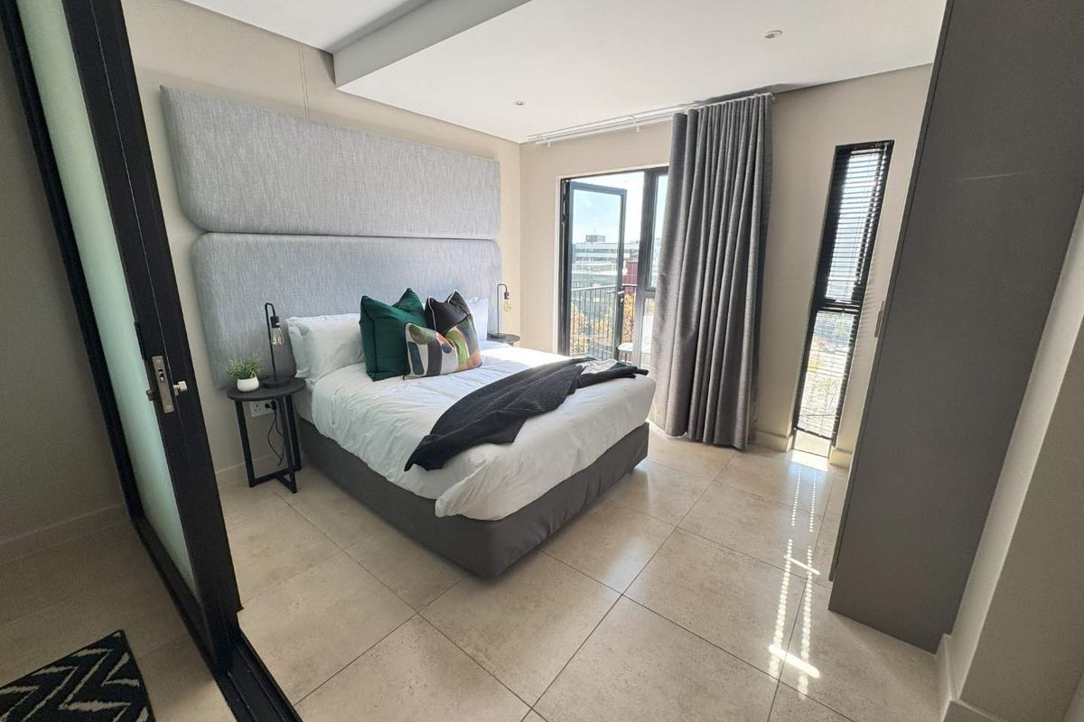 Modern bedroom featuring a large upholstered headboard, tiled flooring, recessed ceiling lighting, and a sliding glass door leading to a balcony.
