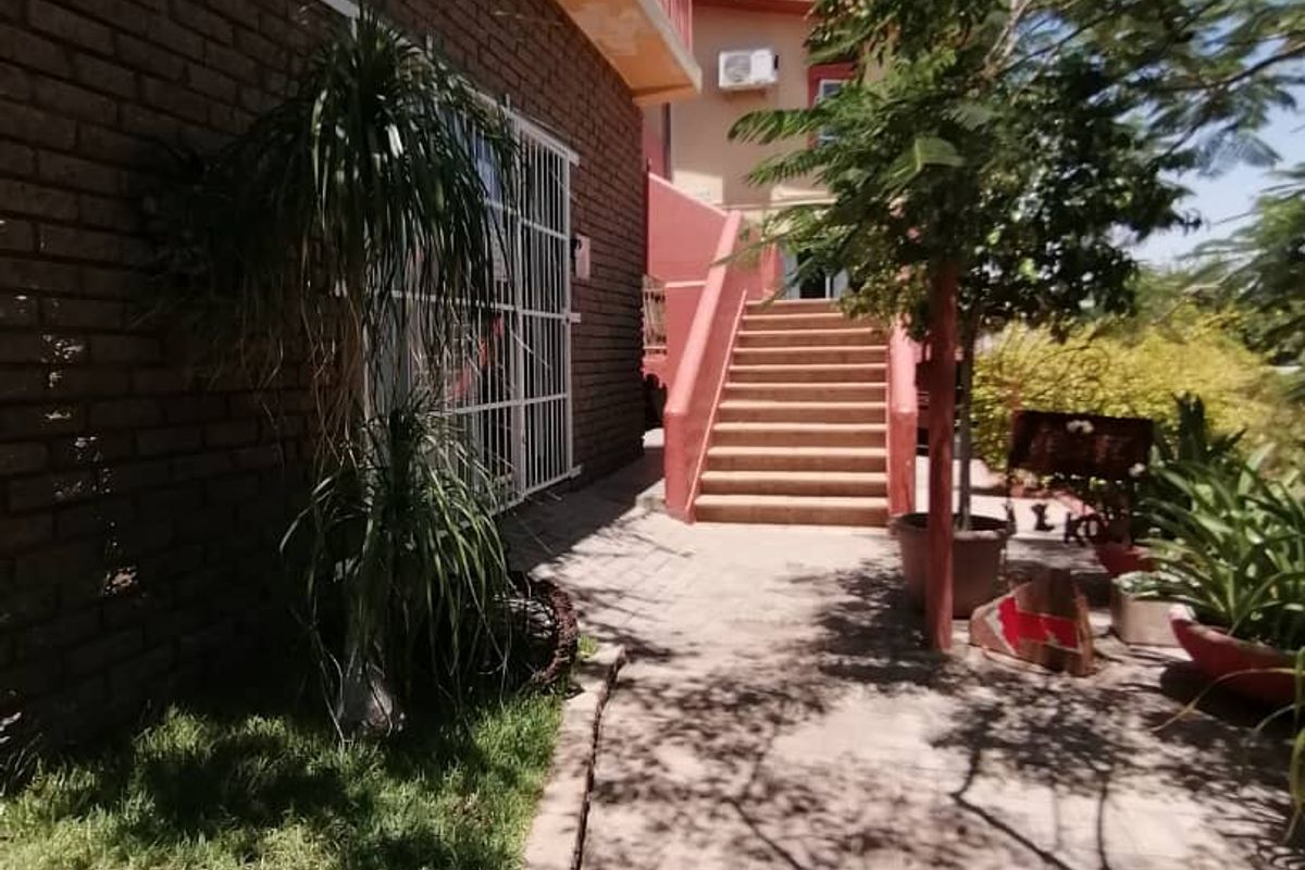 Exterior view of the guest house featuring a paved walkway, brick facade, and an external staircase leading to the upper level.