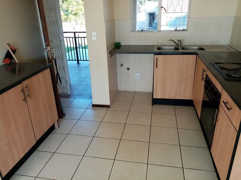 A functional kitchen featuring light wood cabinetry, granite countertops, a double sink, and tiled flooring, with direct access to an outdoor balcony area.