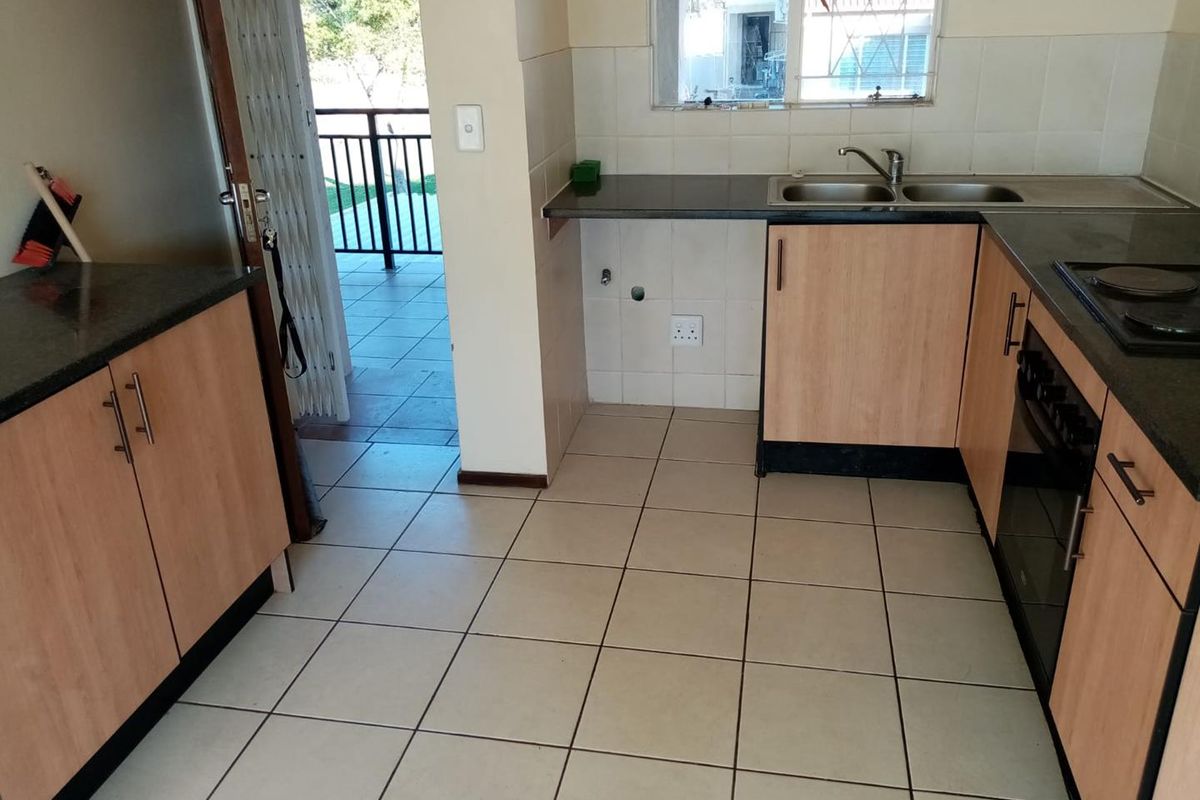 A functional kitchen featuring light wood cabinetry, granite countertops, a double sink, and tiled flooring, with direct access to an outdoor balcony area.