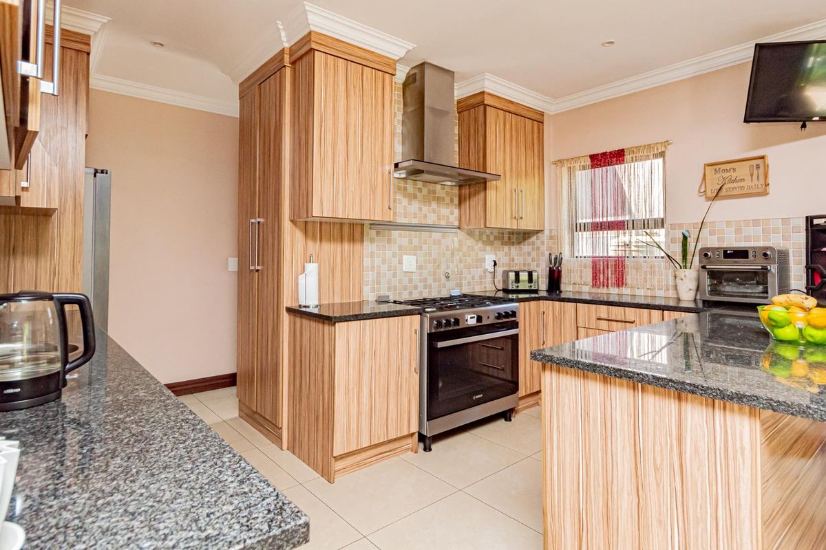 A well-maintained kitchen featuring wood-grain cabinetry, granite countertops, a stainless steel extractor fan, and a built-in oven with gas hob.