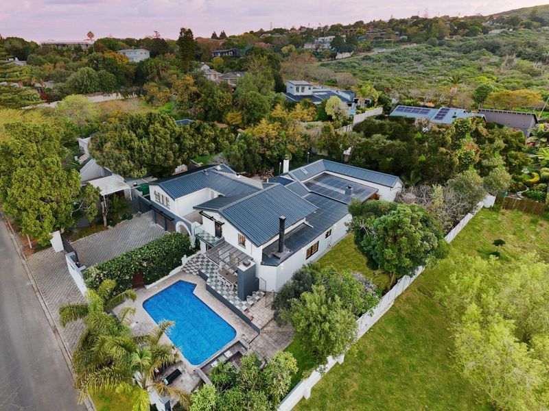 Aerial view of a residential property featuring a swimming pool, paved patio area, metal roofing with solar panels, and established garden surroundings.